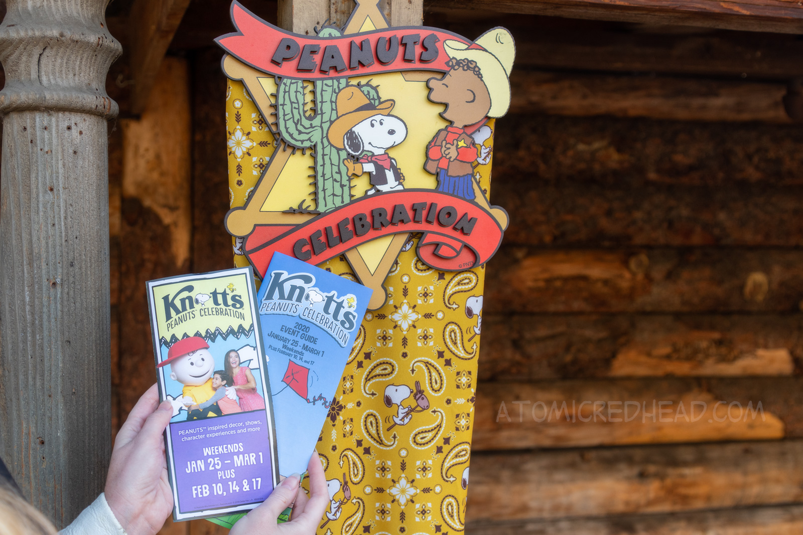 A sign featuring Snoopy and Franklin dressed as cowboys. Text reads "Peanuts Celebration" in front of the sign my hands hold a map and a guide for the Celebration.