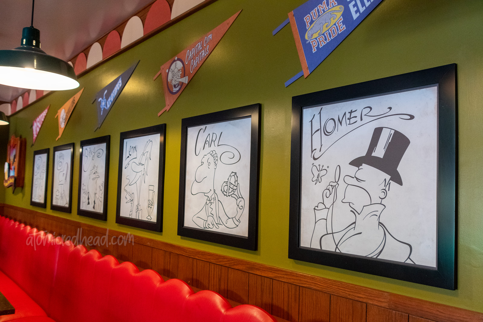 Cartoon illustrations of Homer and his buddies line the wall of Moe's.