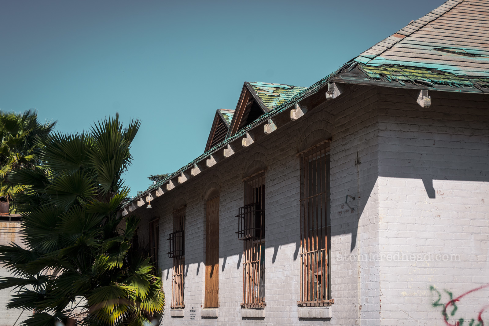 An abandoned building of brick that has been painted white. The windows have rusting bars over the windows. 