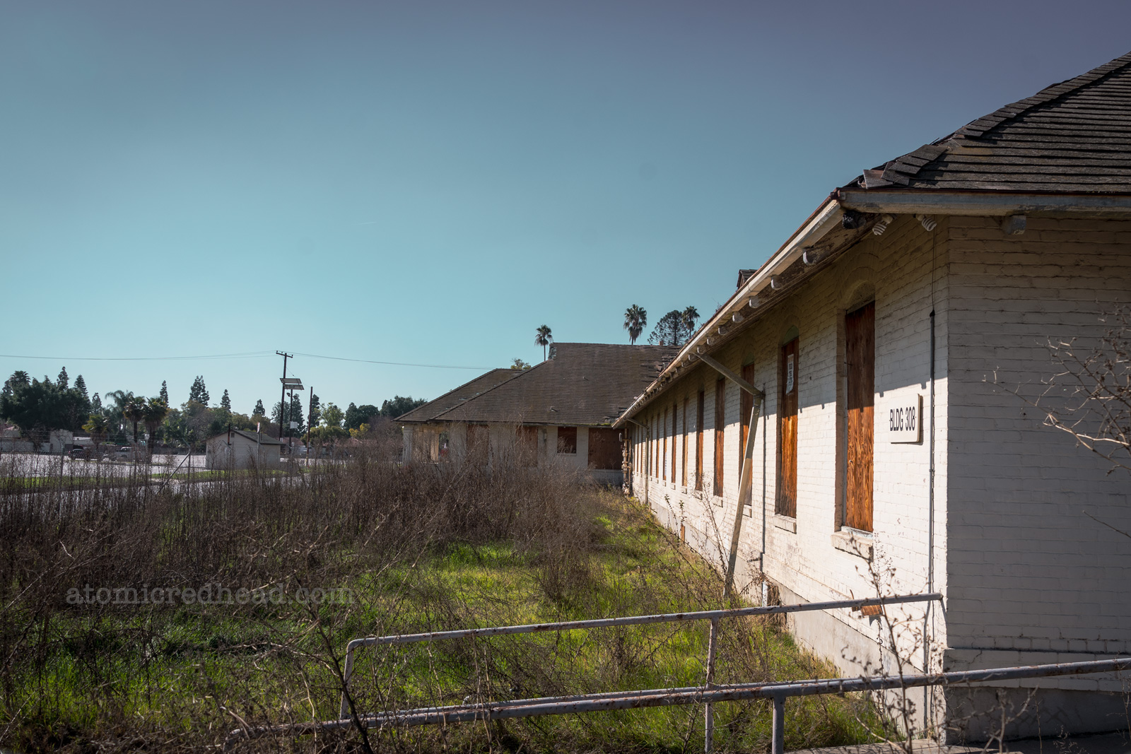 A long, single story building of white brick has boarded up windows.