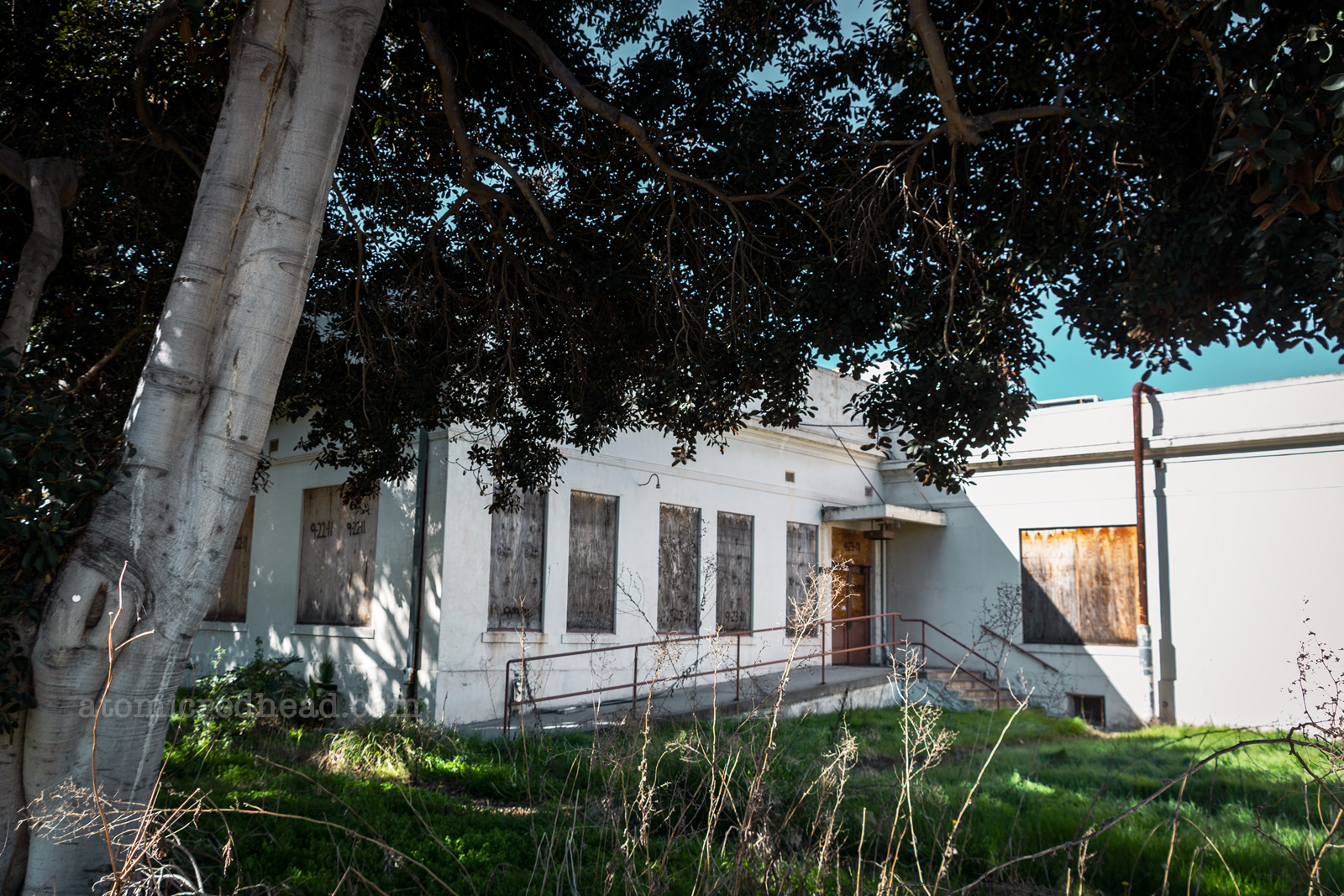 An industrial flat roofed building has a ramp up to a boarded up door. All of the windows have been boarded up as well.
