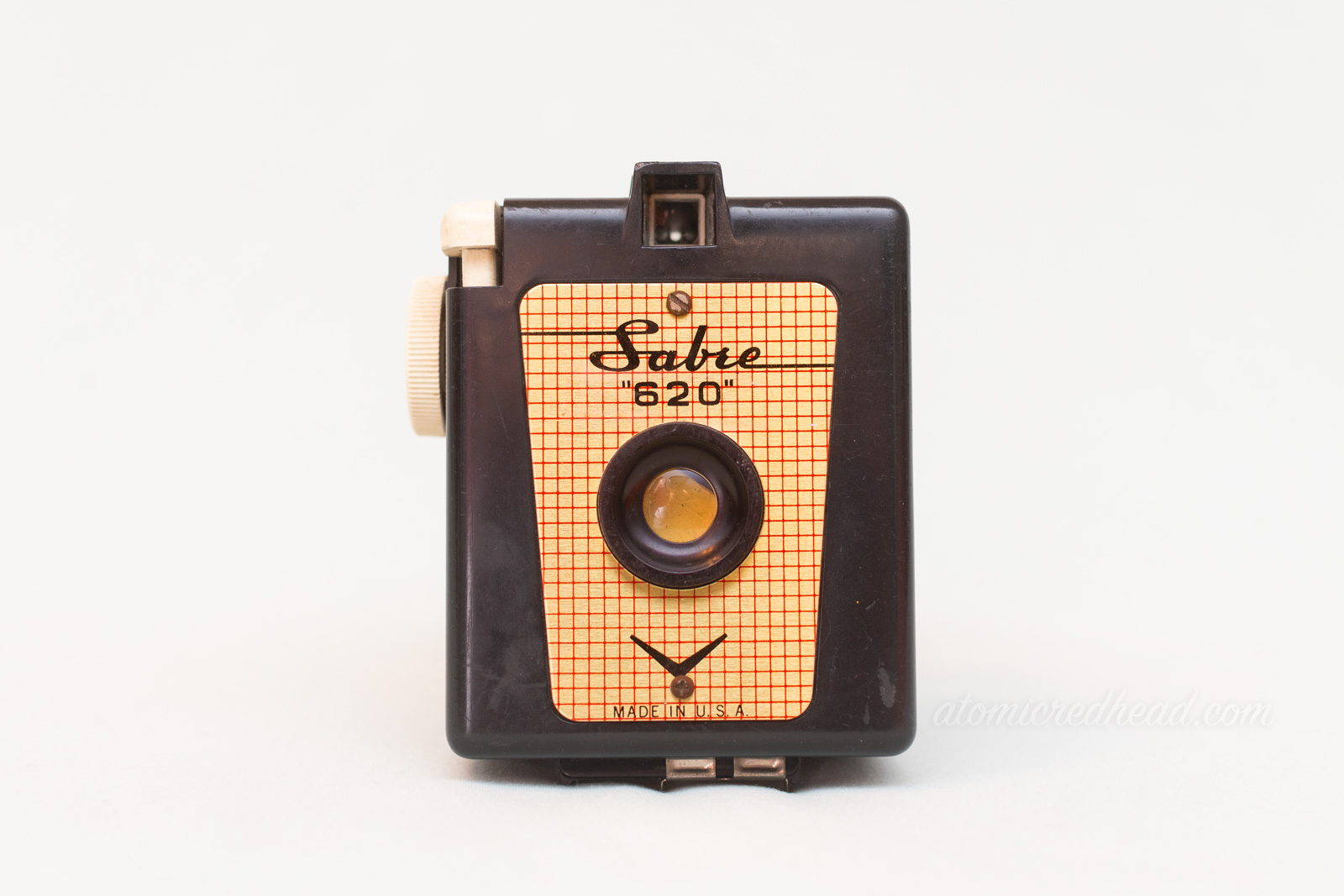 Sabre 620. A black square camera with a gold plate on the front. Black script reads "Sabre"
