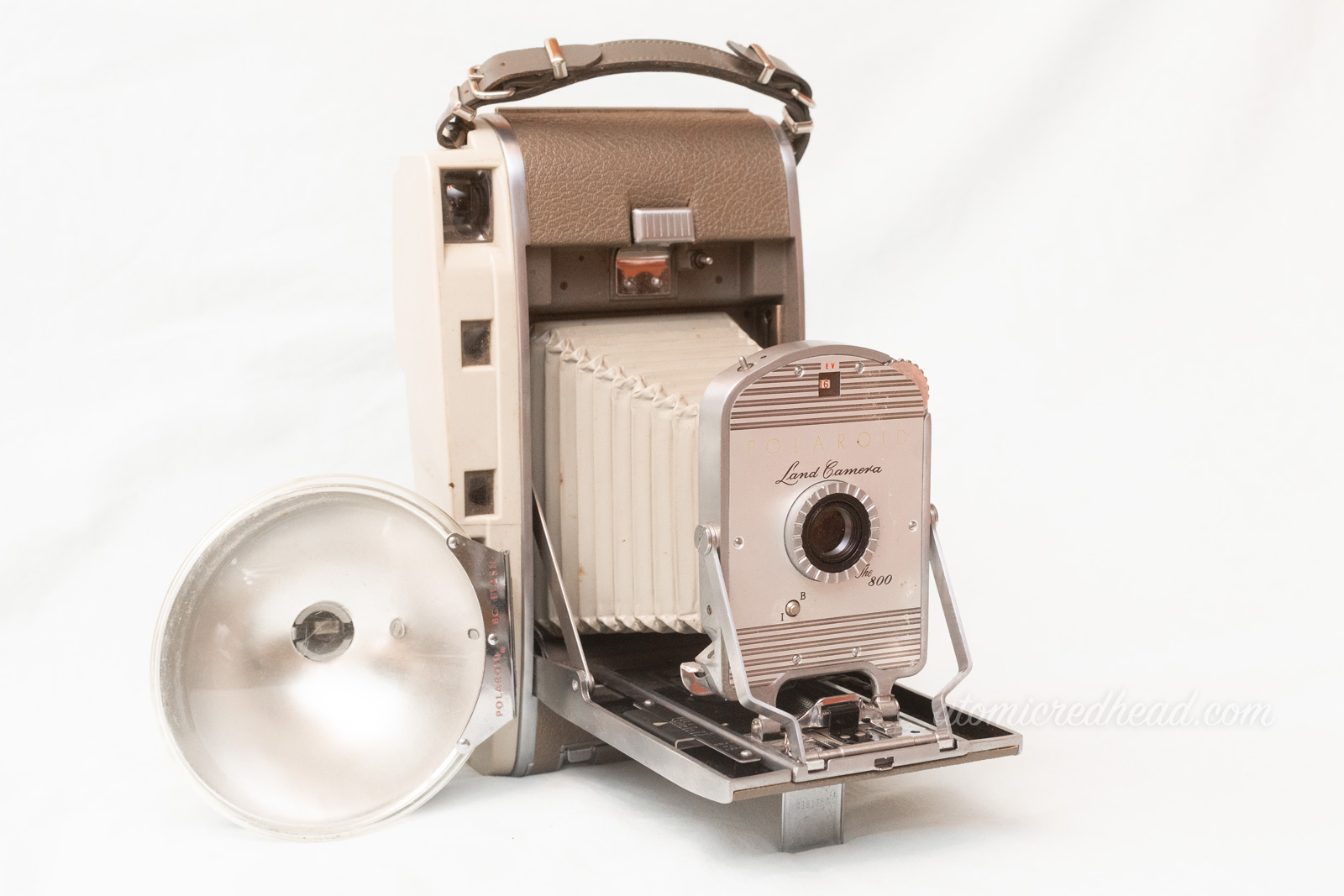 Polaroid Land Camera 800. A two tone grey camera with a bellows and a flash attachment.