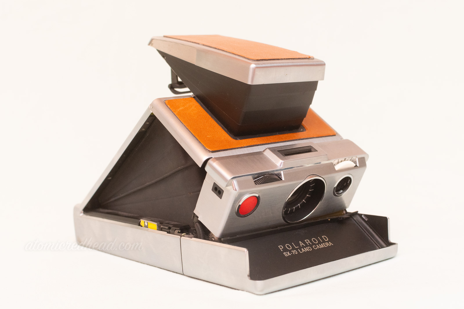 SX-70 Land Camera. The camera pops up like a tent. It features tan leather on the top and grey metal around the edges.