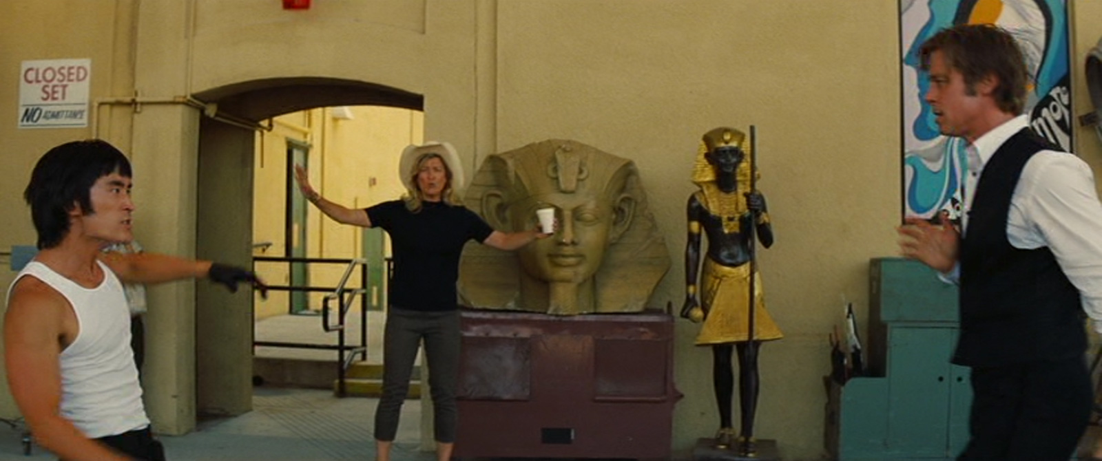 Janet, woman wearing black mock turtle neck short sleeve short, olive capris, and a straw cowboy hat steps in front of a Sphinx head.