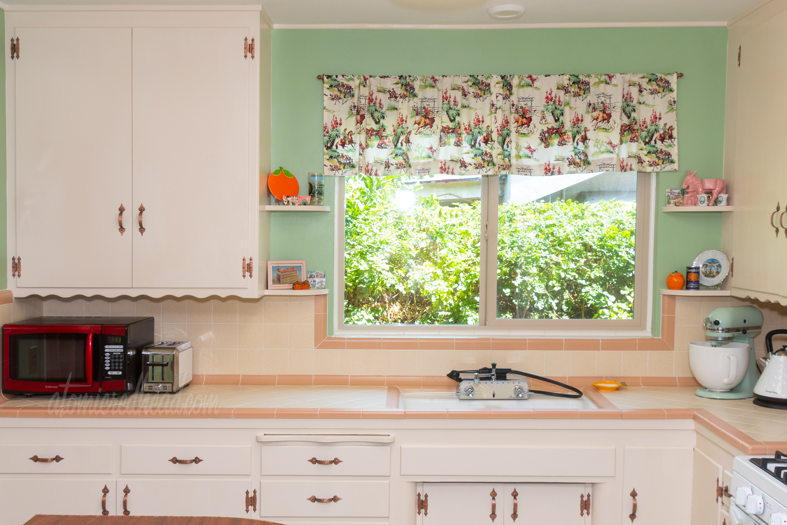 Direct view toward the sink. On either side of the window above the sink are small shelves which have various vintage orange and California souvenirs on them.