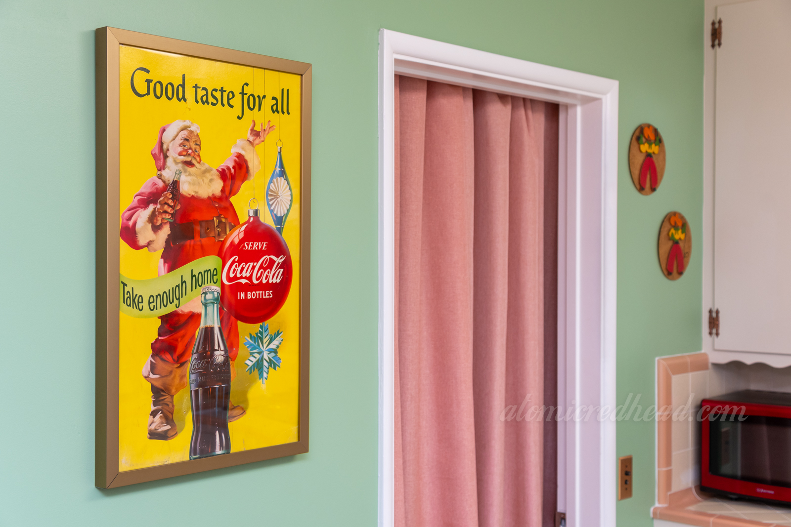 A framed Coca-Cola advertisement featuring Santa reading "Good taste for all" hangs on our kitchen wall.