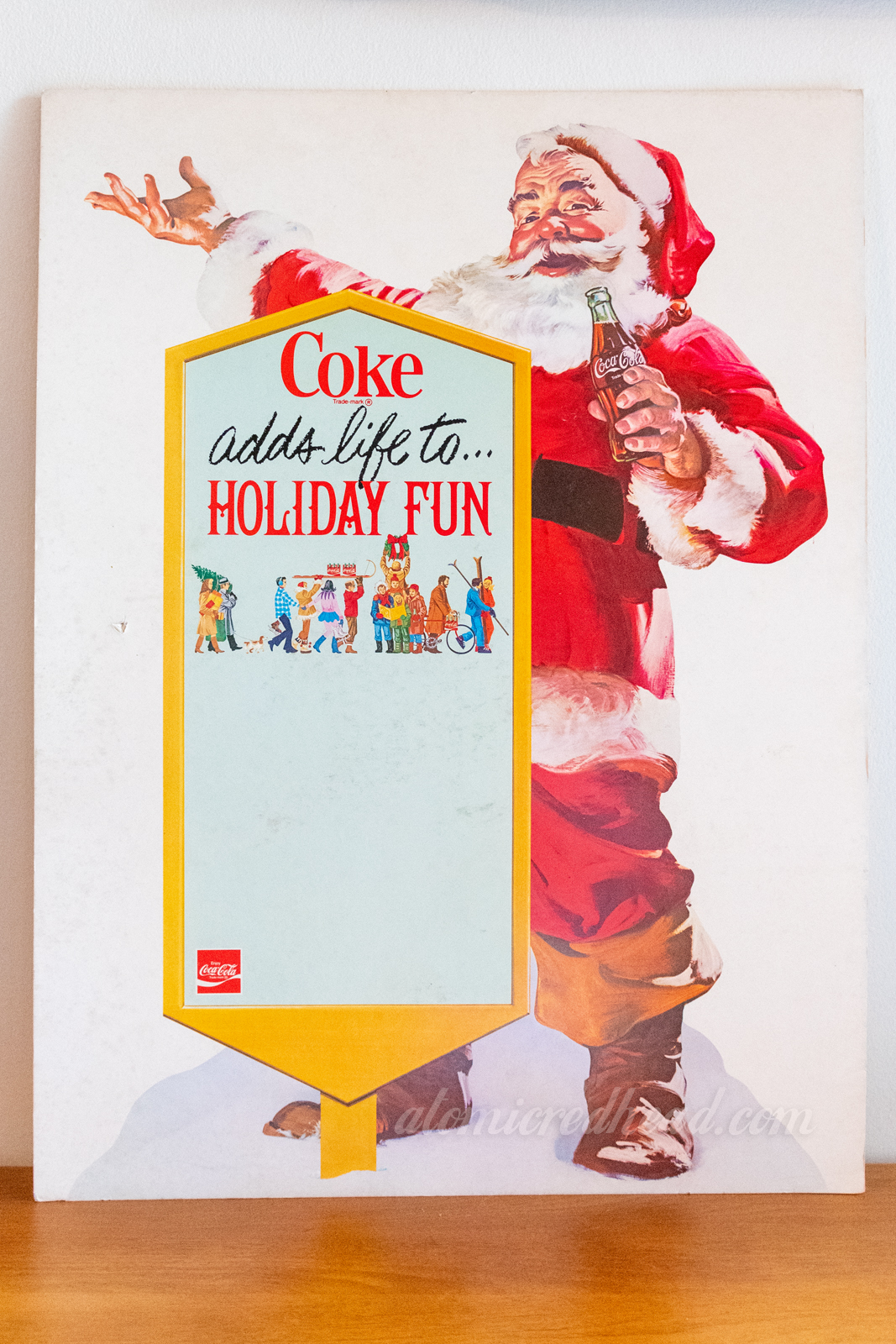 A cardboard advertisement of Santa next to a sign that reads "Coke adds life to Holiday Fun"