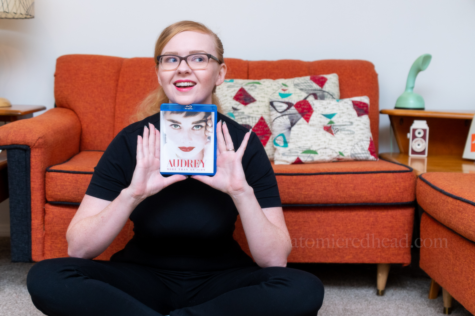 Myself, sitting on the floor, wearing a short sleeve black mock-turtle neck, and black pants,