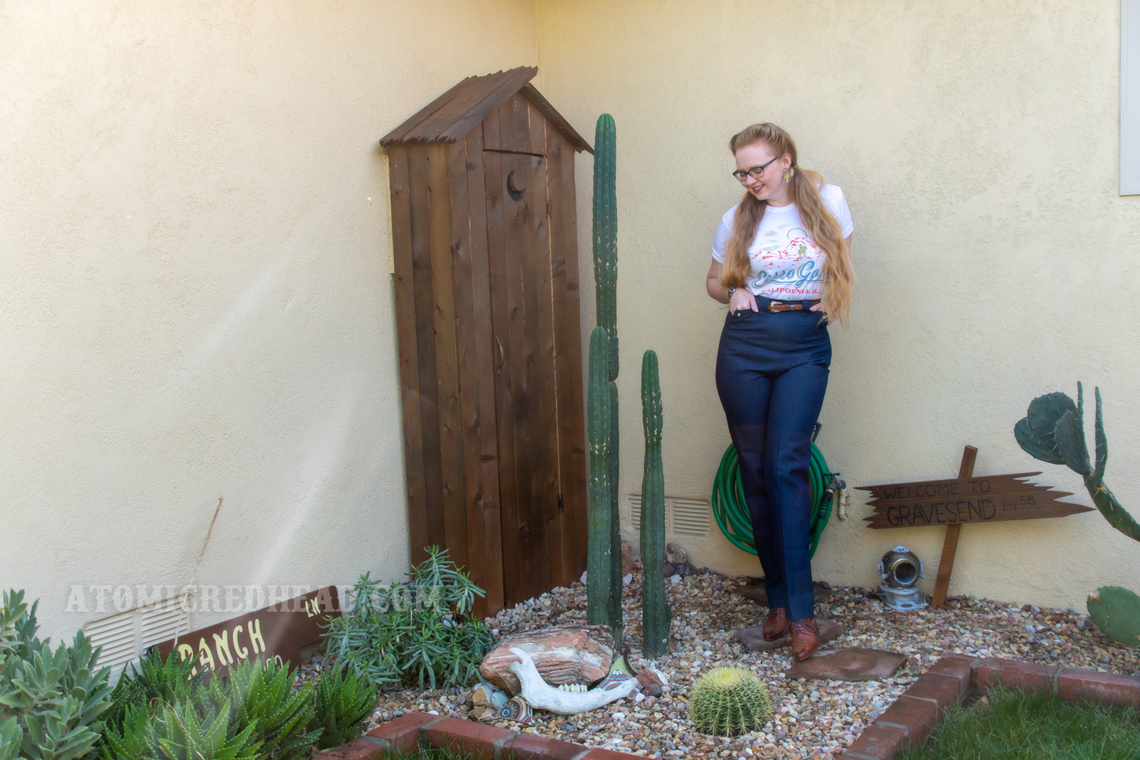 Myself standing in front of a western style outhouse with cacti in front, wearing a Cerro Gordo tee and western style jeans.