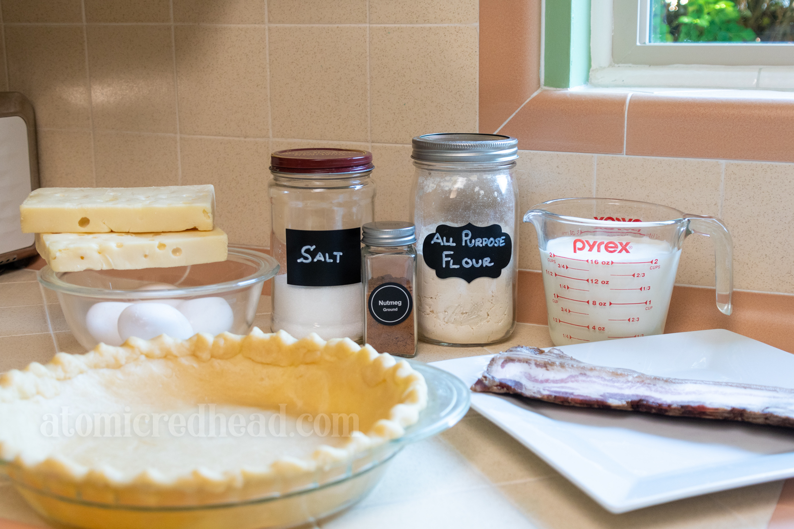 Ingredients, including a pie shell, cheese, eggs, salt, nutmeg, flour, milk, cream, and bacon.