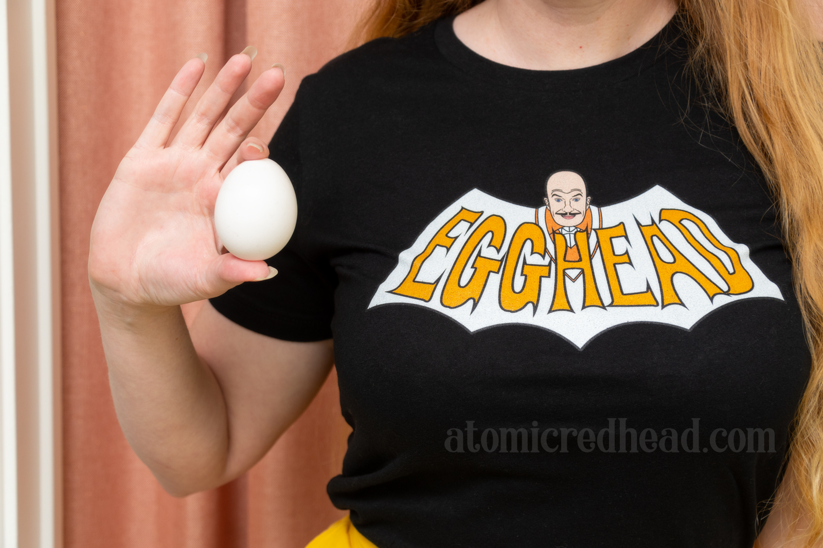 Close-up of my shirt, which reads "Egghead" in a bat shape, with the bald head of the character of Egghead at the top, in my hand is an egg.