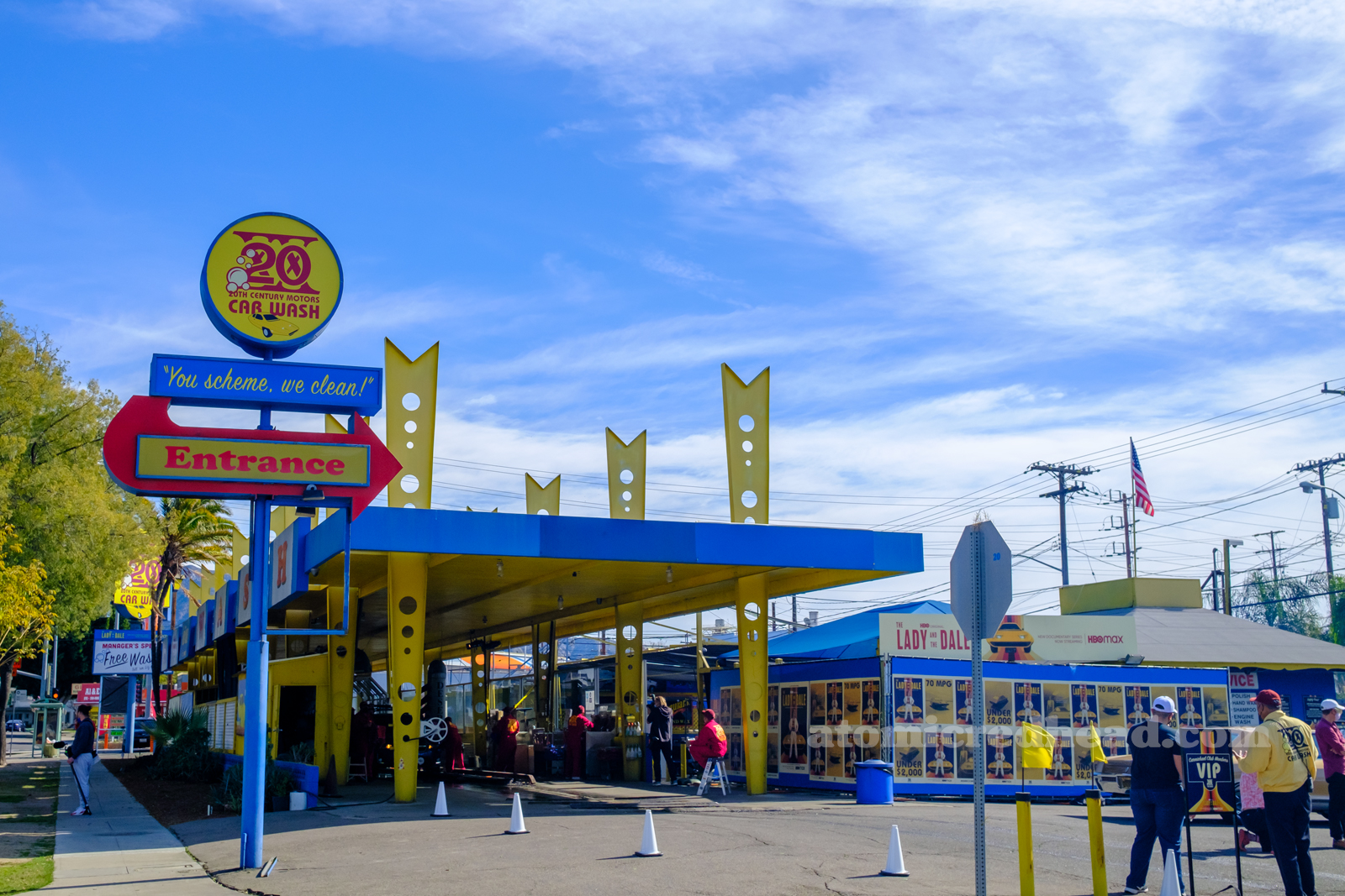 Cars exit the car wash, which features a blue roof and a yellow posts.