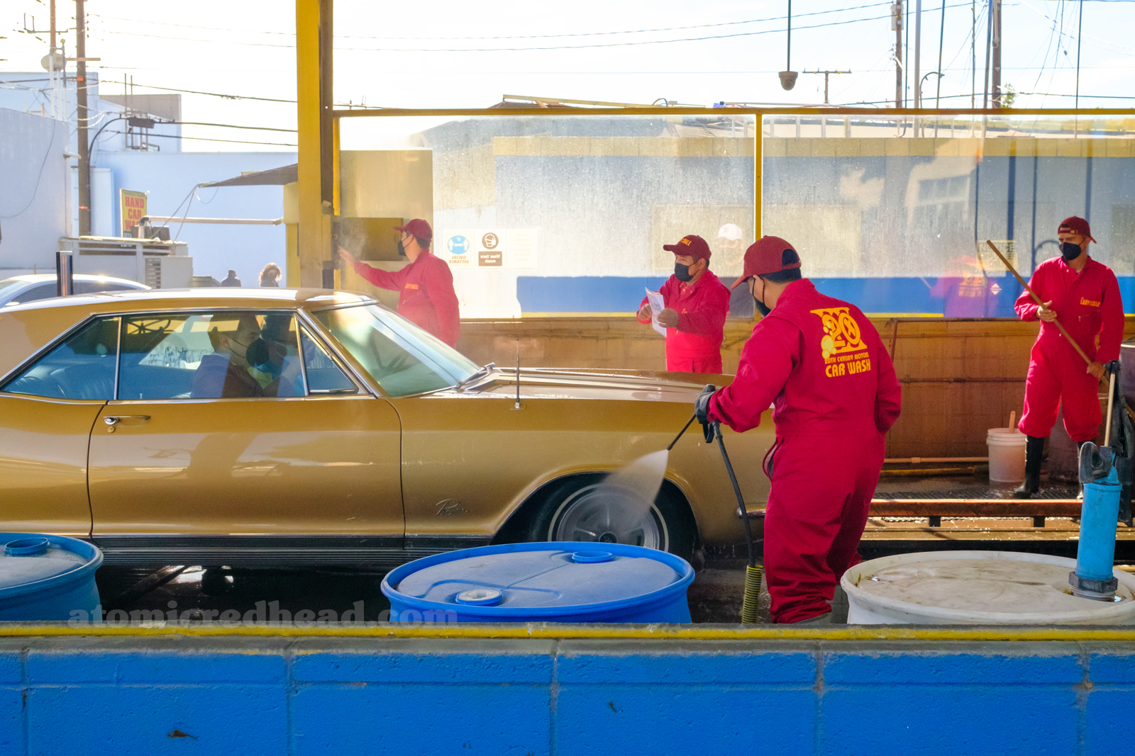 A gold Buick Rivera enters the car wash, employees in red coveralls with yellow text reading "20th Century Motors"