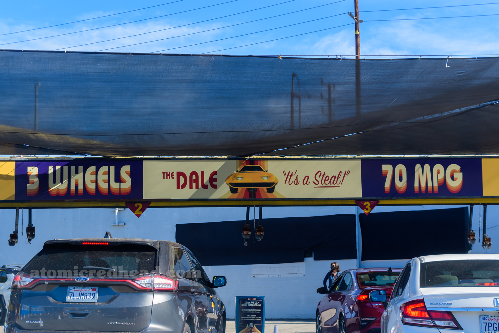 Banner across the entrance to the car wash, "3 Wheels, The Dale 'It's a Steal' 70 MPG"
