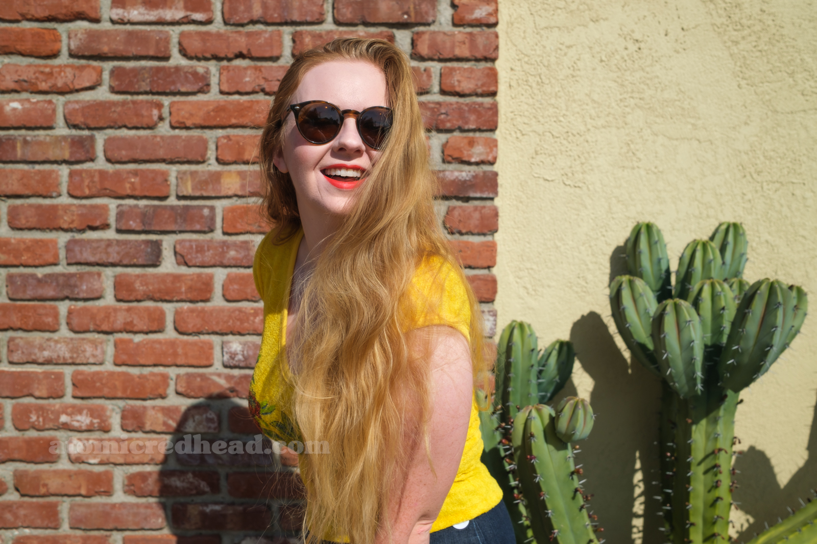 Myself, wearing a yellow terrycloth shirt featuring red hibiscus flowers and a parrot, blue wide leg jeans, red platform shoes, standing outside against a brick wall.