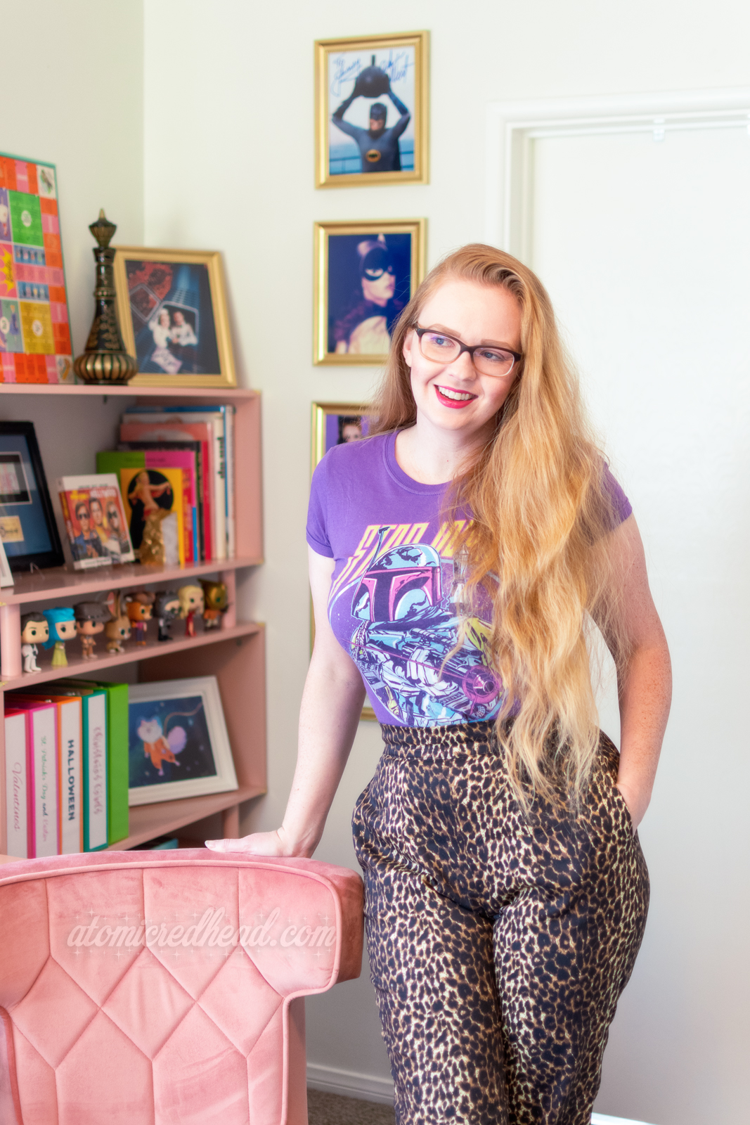 Myself, wearing a purple Boba Fett Star Wars tee, and leopard print pants, leaning against a pink velvet chair.