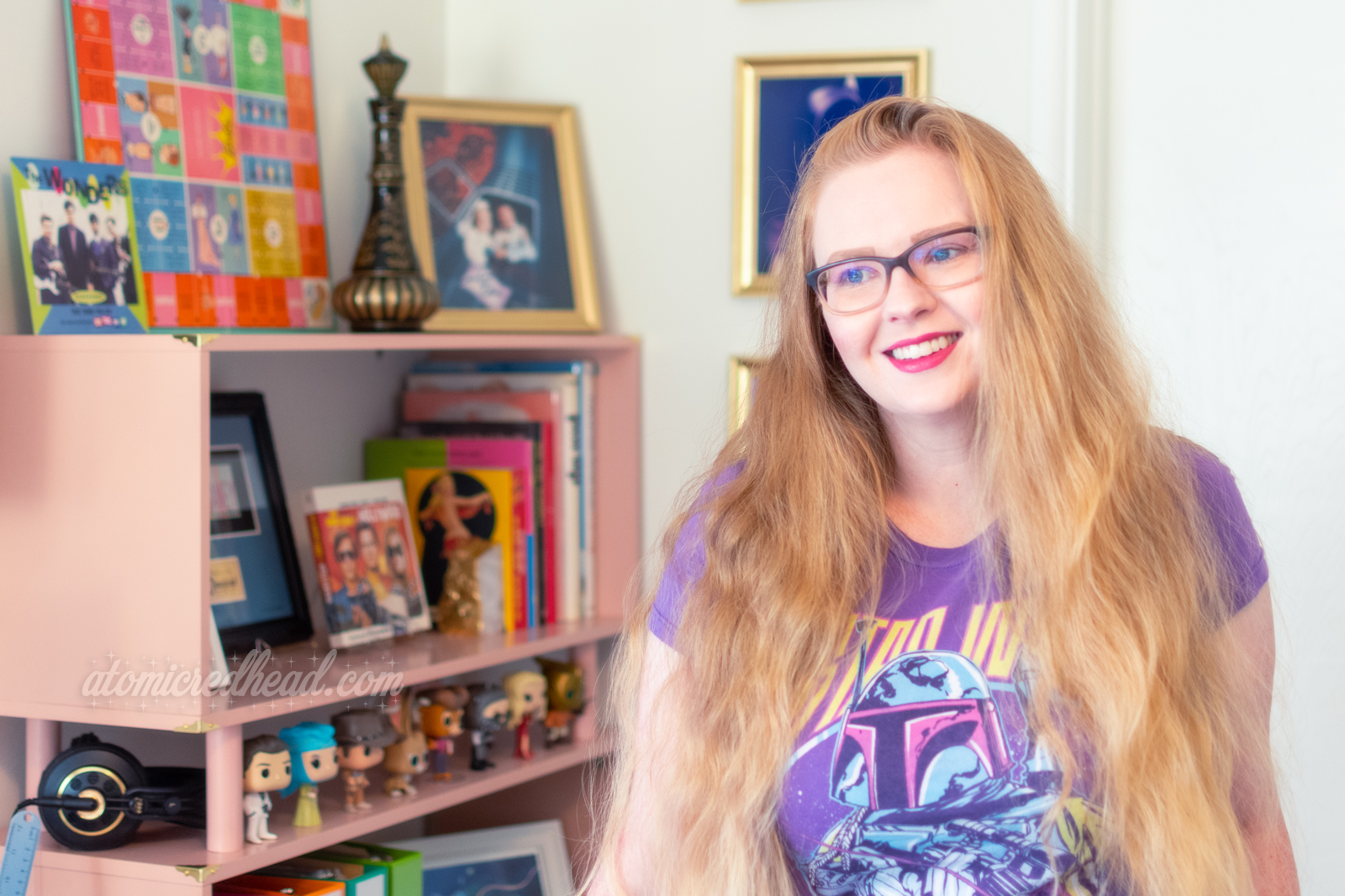 Myself, standing in front of a pink bookcase, wearing a purple Boba Fett shirt.