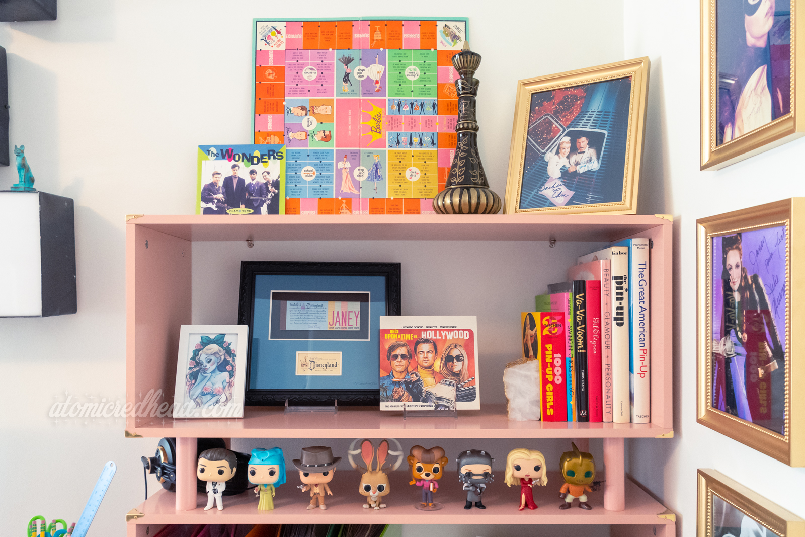 Shot of my bookcase. Various autographs hang on the wall, a collection of Funko Pops sit on the shelf along.