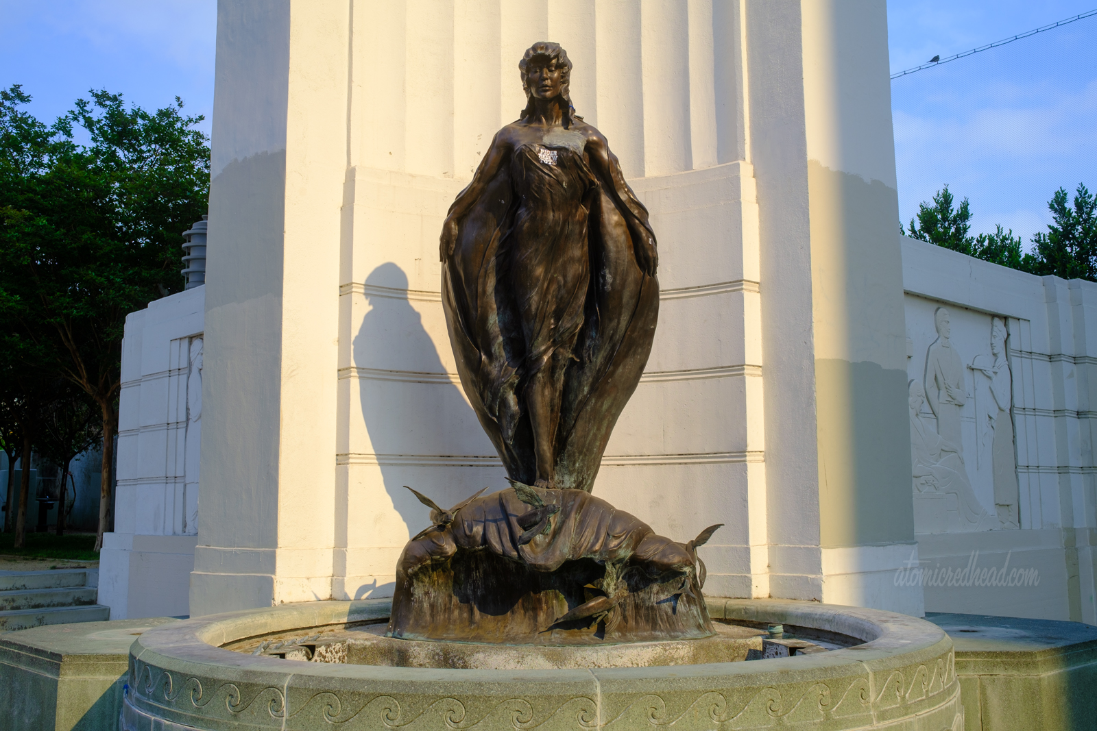 A statue of a woman who rides a small wave with flying fish emerging from it.