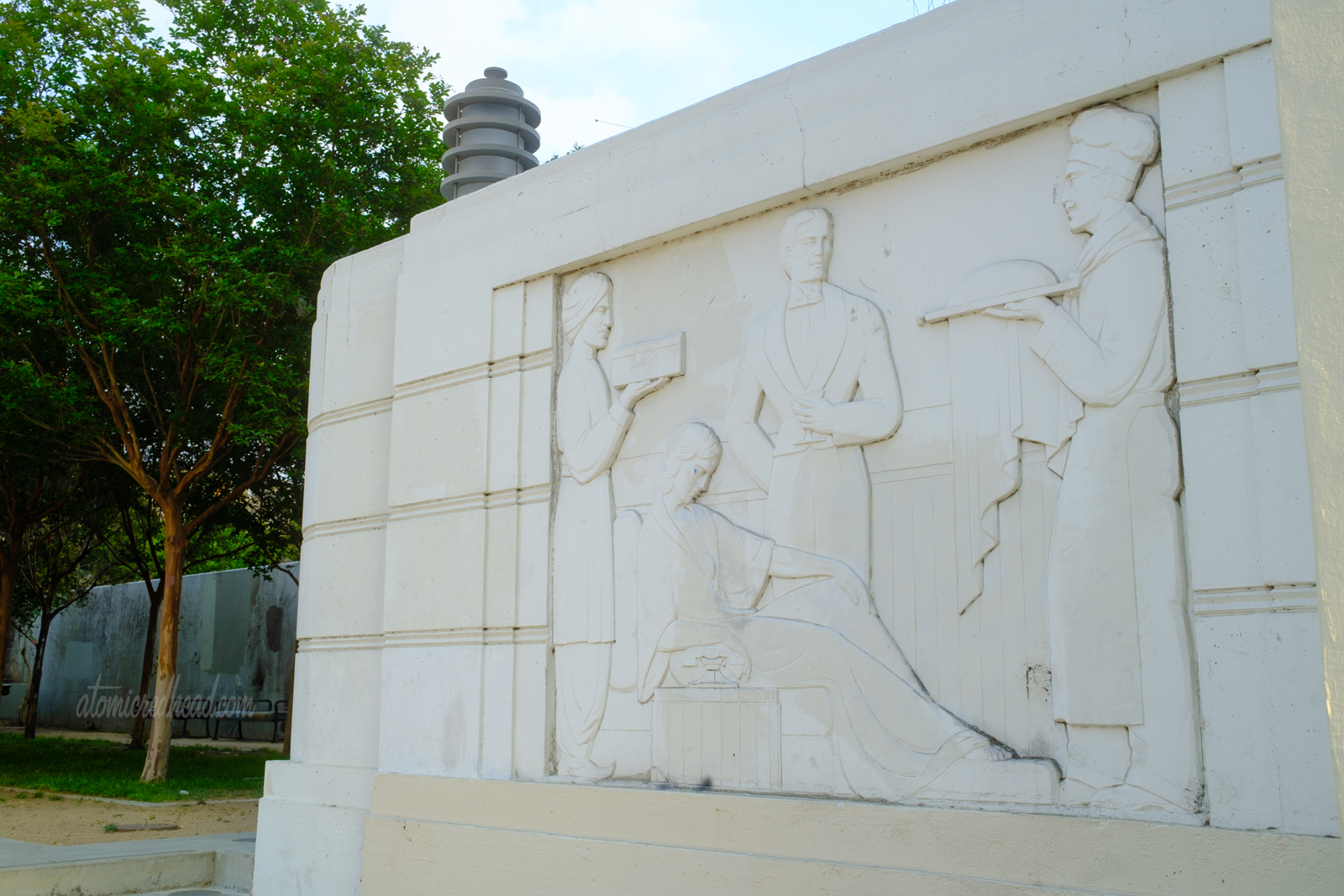 Carved into a small wall is an Art Deco image of a woman in bed being served by various men.