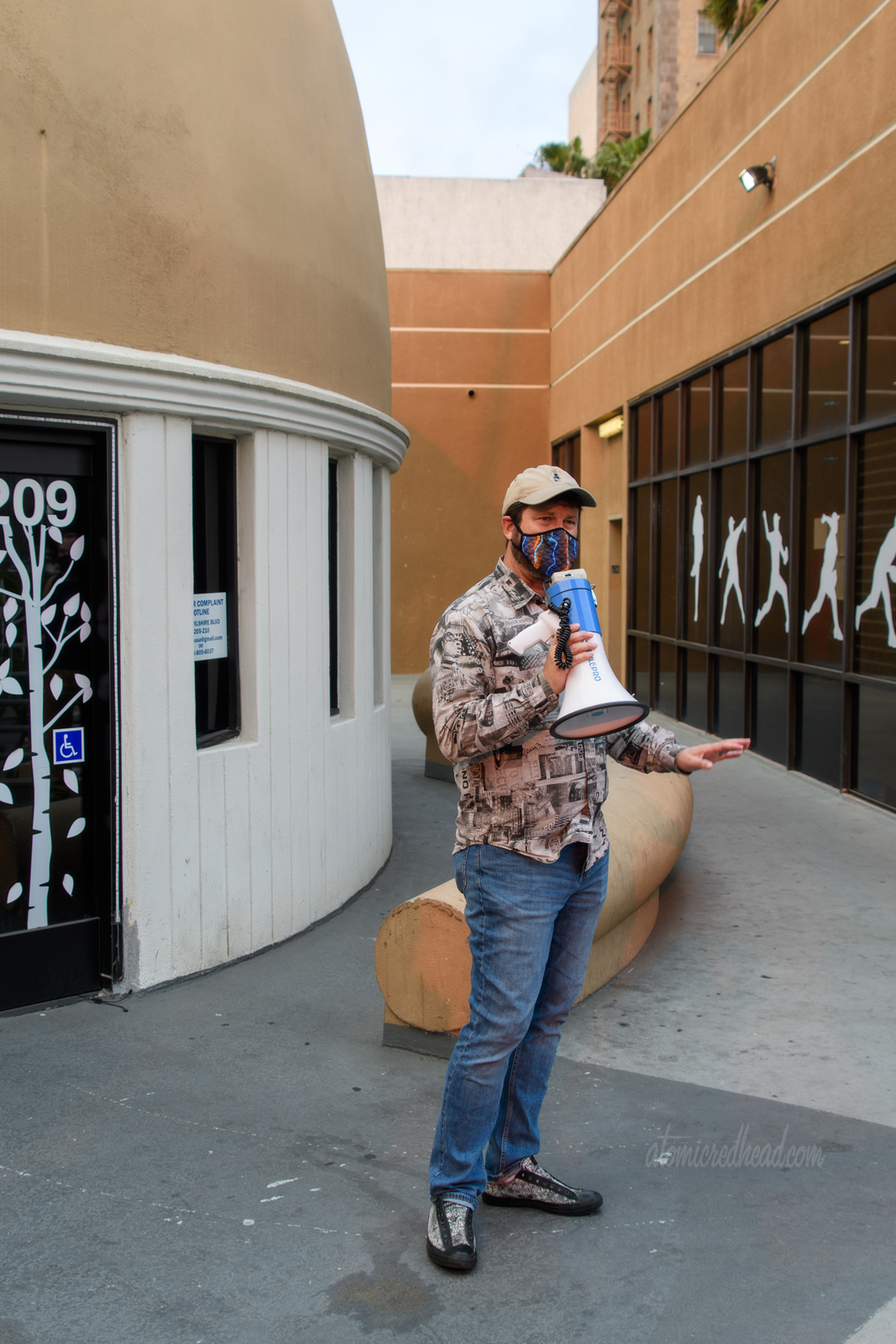 Eric uses a megaphone to talk to those of us on the tour, he wears a shirt made of black and white images of neon signs. Behind him is the old Brown Derby, at his feet includes the brim of the hat.