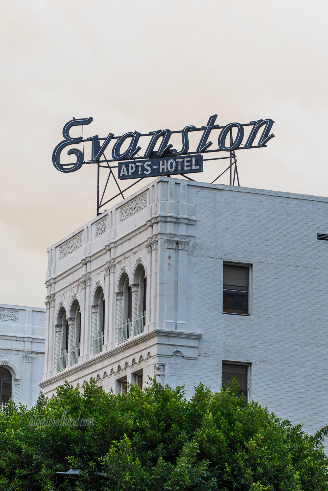 An Italianate designed apartment building painted white. Atop the roof in elegant script reads "Evanston" with a smaller sign below reading "Apts Hotel"