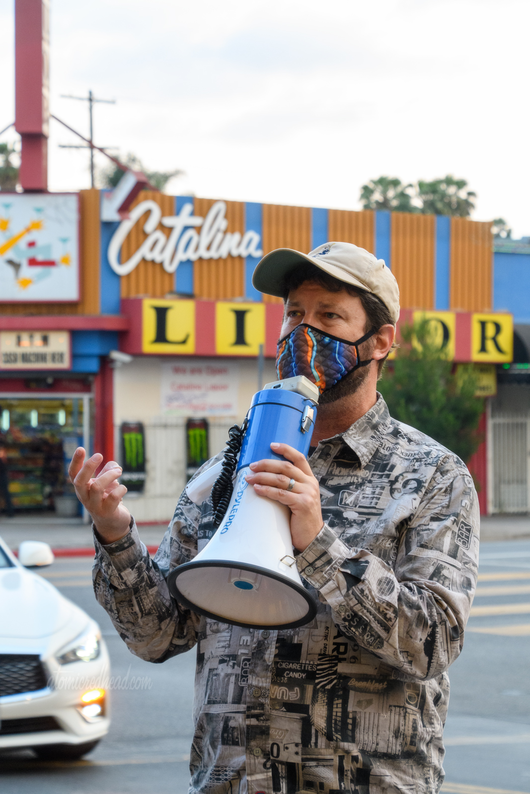 Eric uses a megaphone to talk to those of us on the tour, he wears a shirt made of black and white images of neon signs, behind him is Catalina Liquor.
