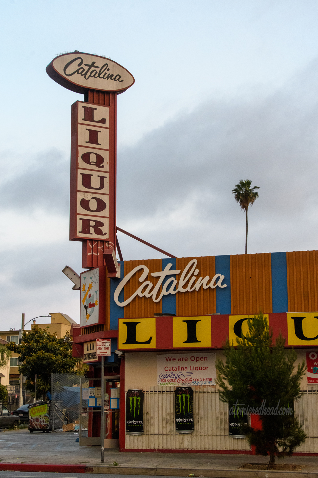 The backlit plastic signs of Catalina Liquor. Catalina is spelled out in an elegant script, while Liquor is spelled out in large yellow blocks with black letters.
