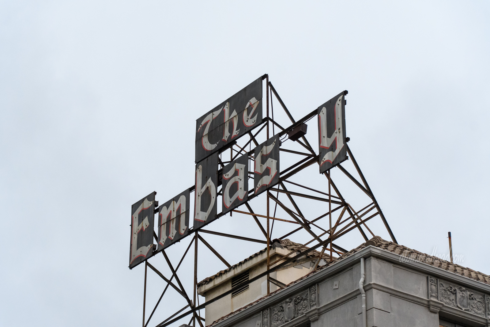 The remains of the sign spelling "The Embassy" however the second "s" is missing.