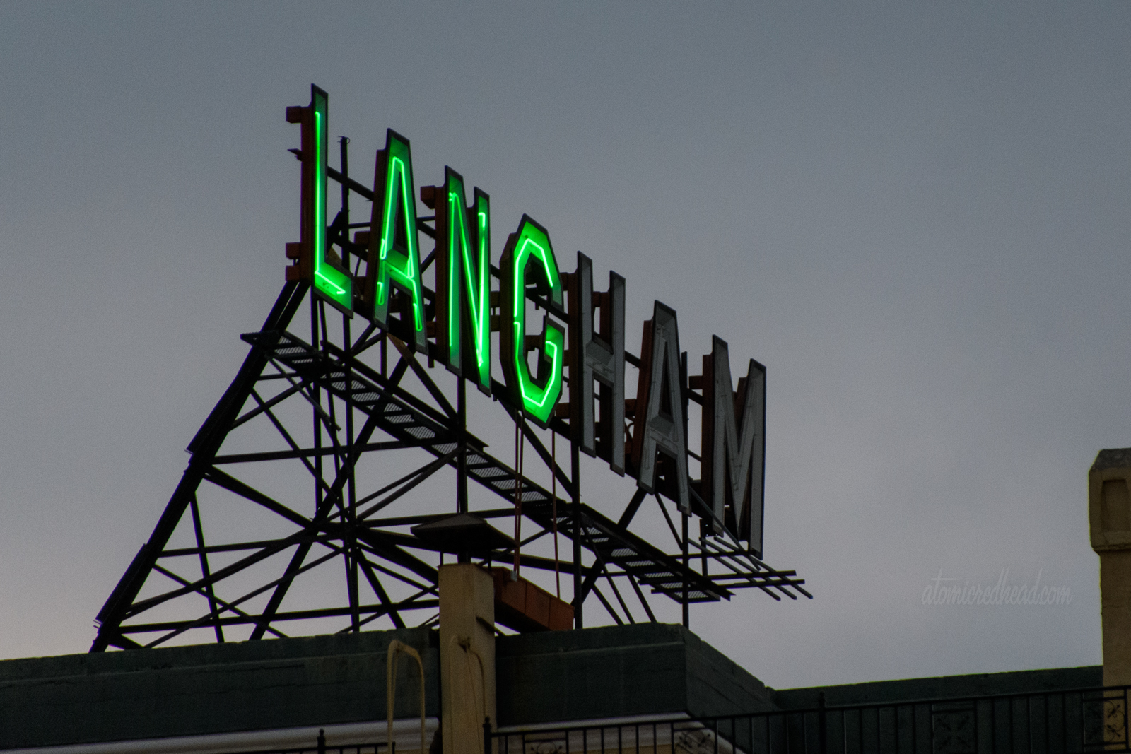 Large neon letters spelled out "Langham" atop a building, however only "Lang" is lit in green neon.