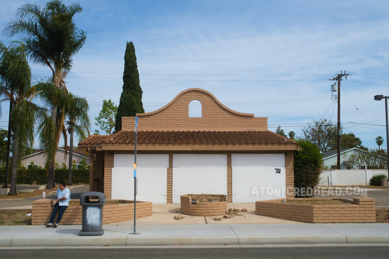 A faded, boarded up former Taco Bell. No signage, no bell. The old fire pit has some broken bricks.