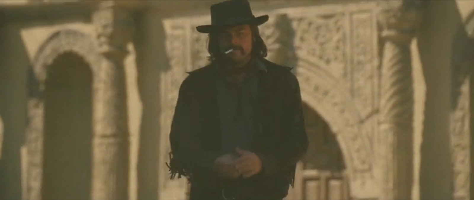 Leonardo DiCaprio walks back to set with a stucco building behind him.