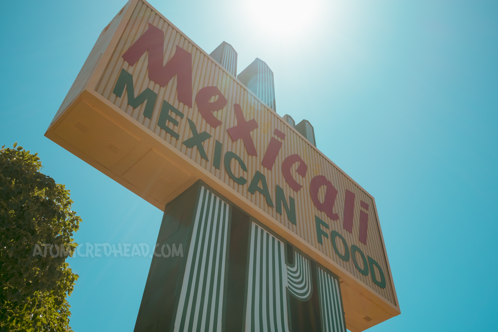 A large backlit plastic cactus rises toward a blue sky. A yellow rectangle crosses the cactus reading "Mexicali Mexican Food"