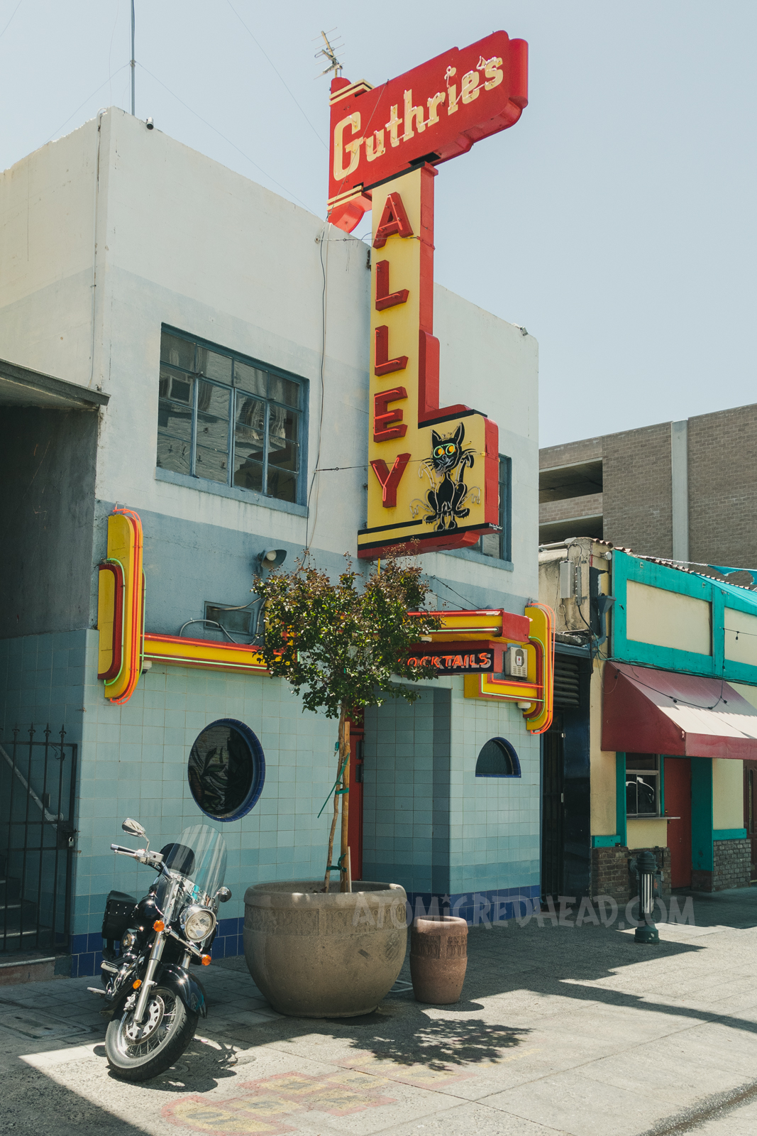 Guthrie's Alley Cat, a small Art Deco style building. The lower half is made up of blue tiles. A neon sign of red and yellow reads "Guthrie's Alley" and then features a small black cat.