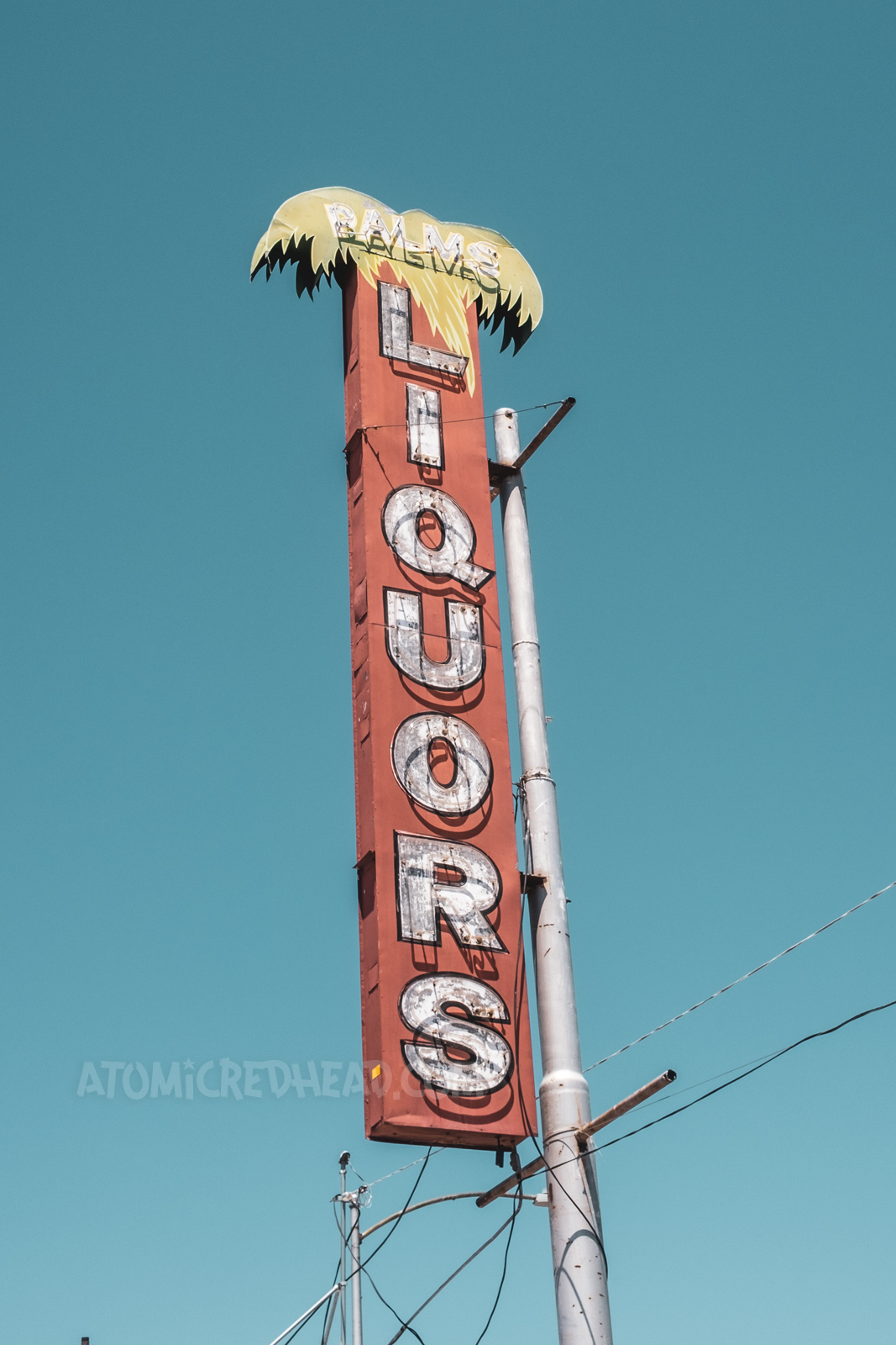 A red neon sign features a palm tree at the top. Letters spell out "Palms Liquors"