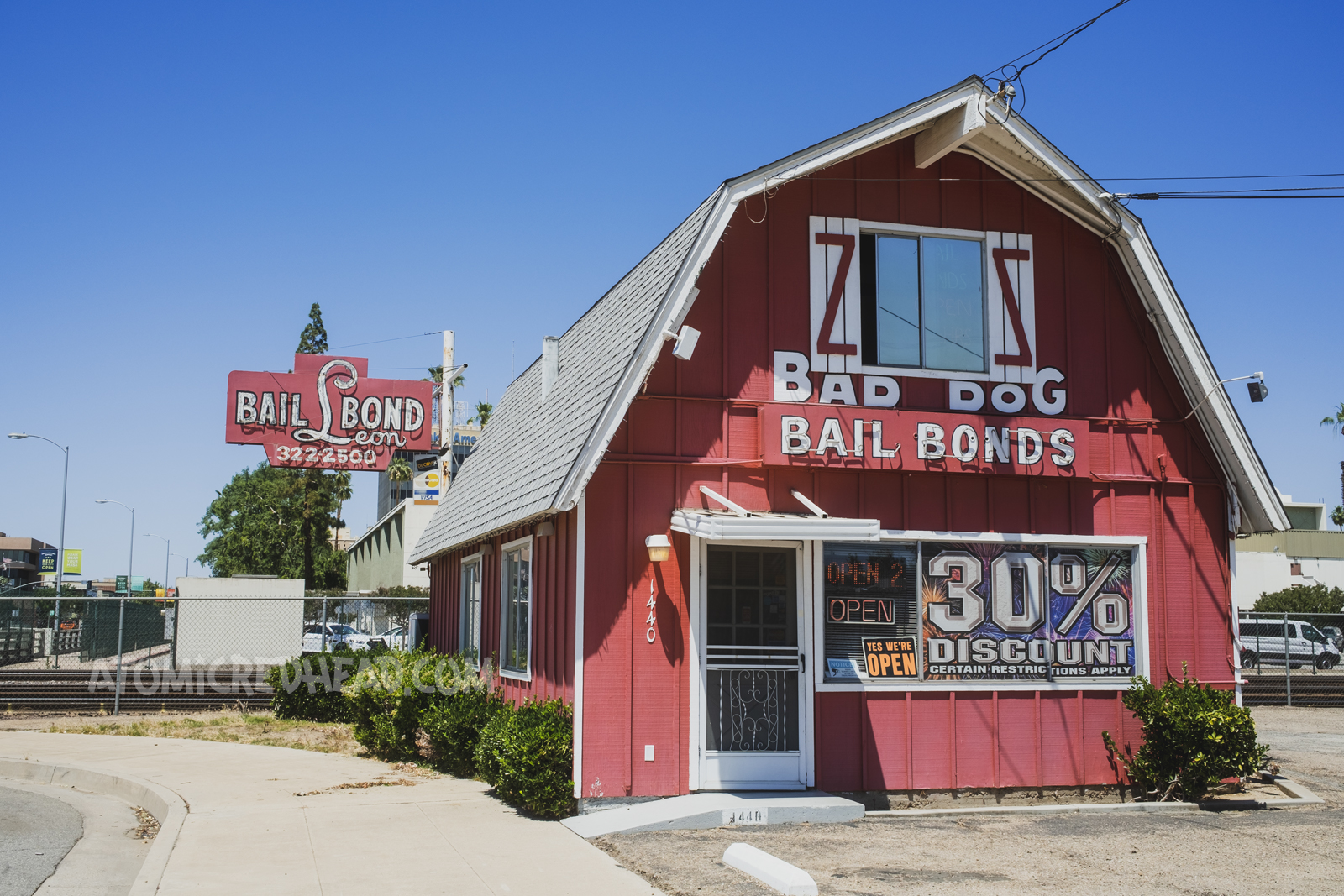 A red barn style building with white trim reads "Bad Dog Bail Bonds" just past the building is a red and white neon sign reading "Bail Bond Leon"