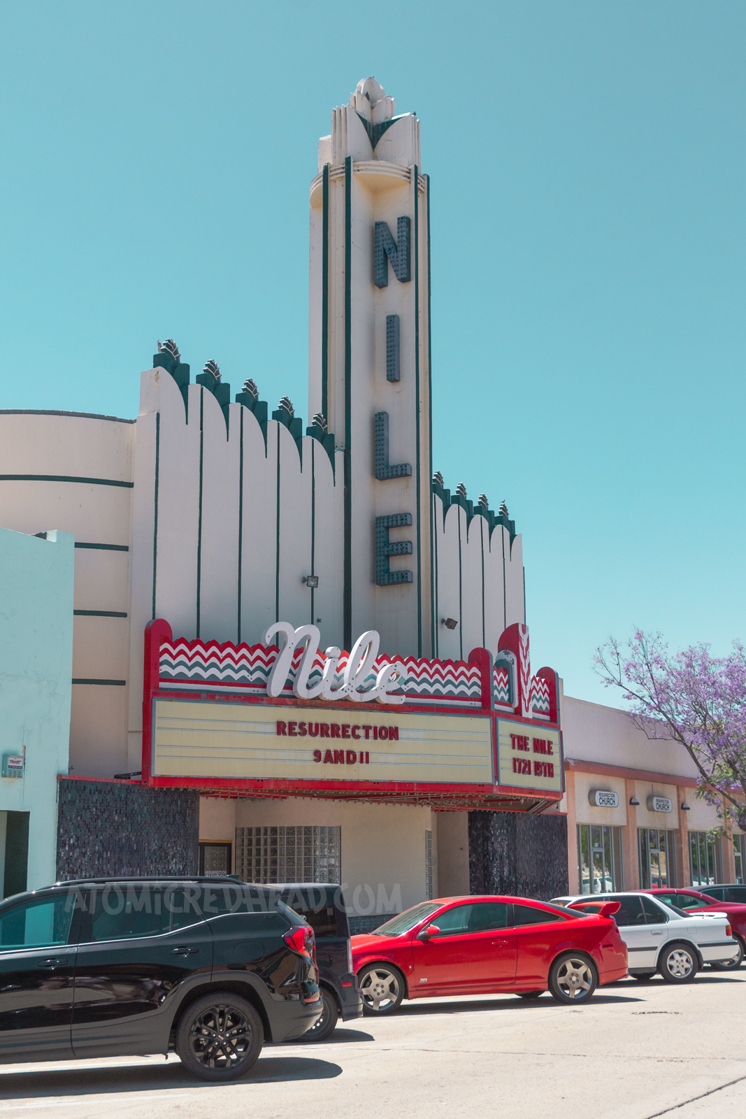 The Nile Theater, an Art Deco style building with a tower in the center reading "Nile" down it in blue letters. The marque features neon and reads "Nile" in cursive white neon.