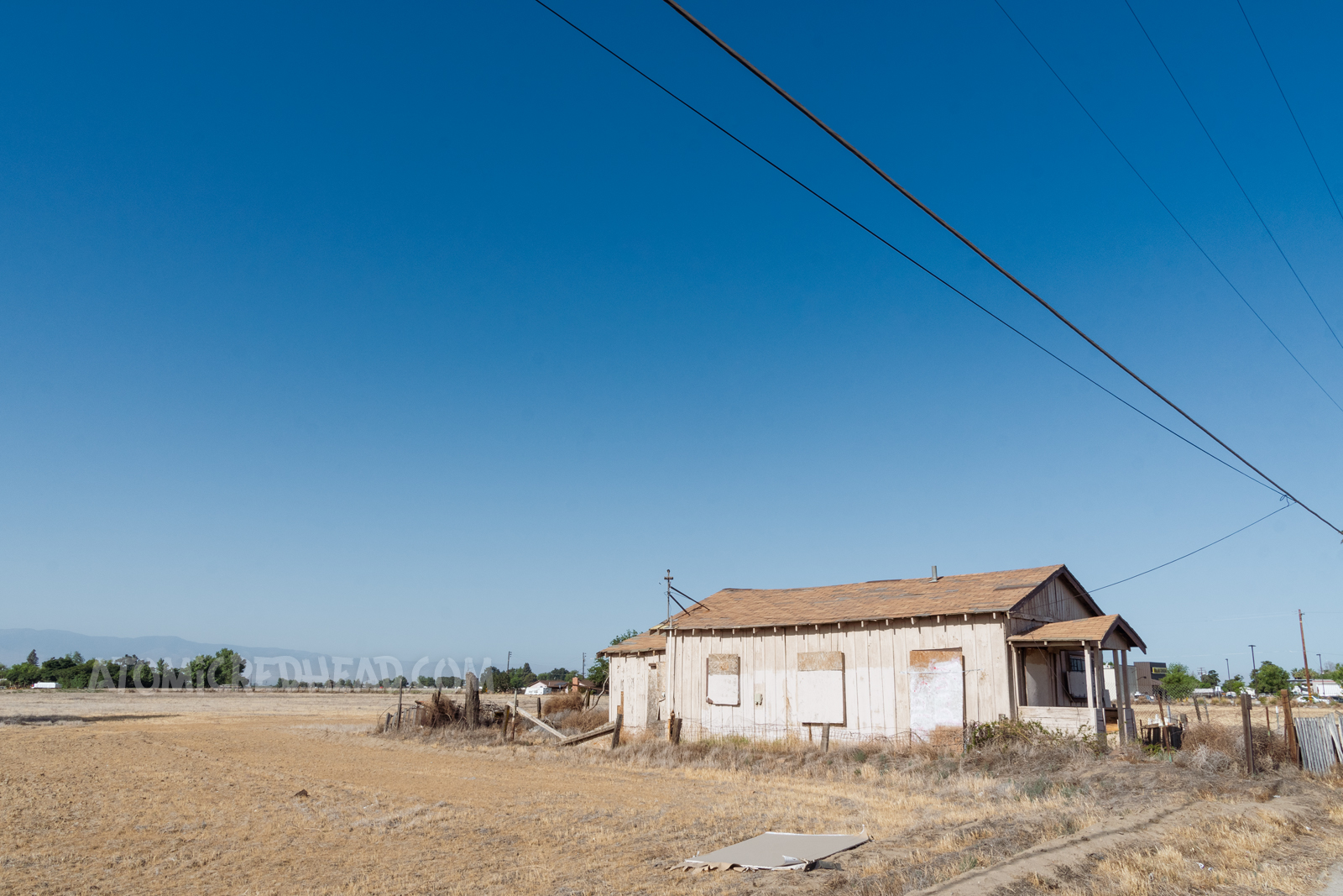 A small dilapidated tan home with boarded up windows. A sprawling dead field stretches out behind it.