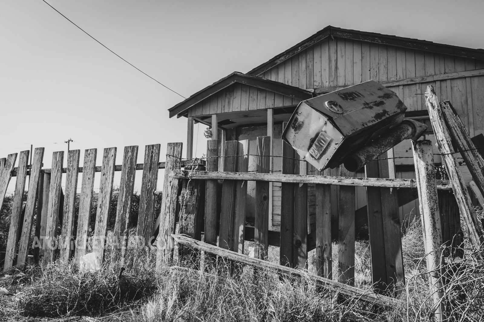 Black and white photo of an abandoned home, its mail box sits, almost about to fall off of its post.