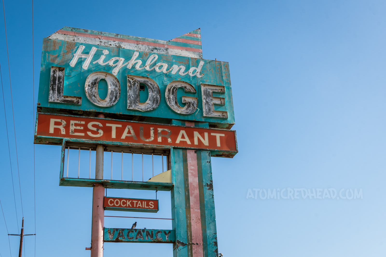 Tall pink, red, and turquoise sign reading "Highland Lodge Restaurant Cocktails" Various parts are faded and flaking. A portion below is missing.