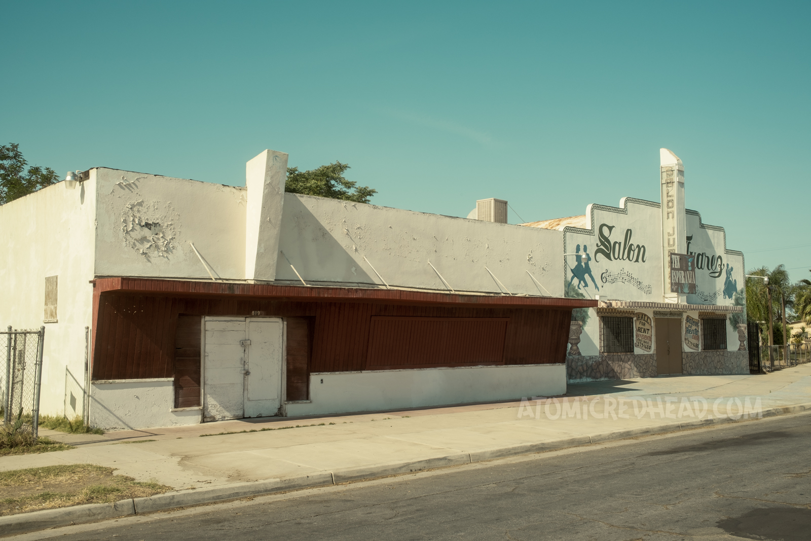 An abandoned storefront or bar, white stucco makes up the upper part, while the middle is of red painted wood.