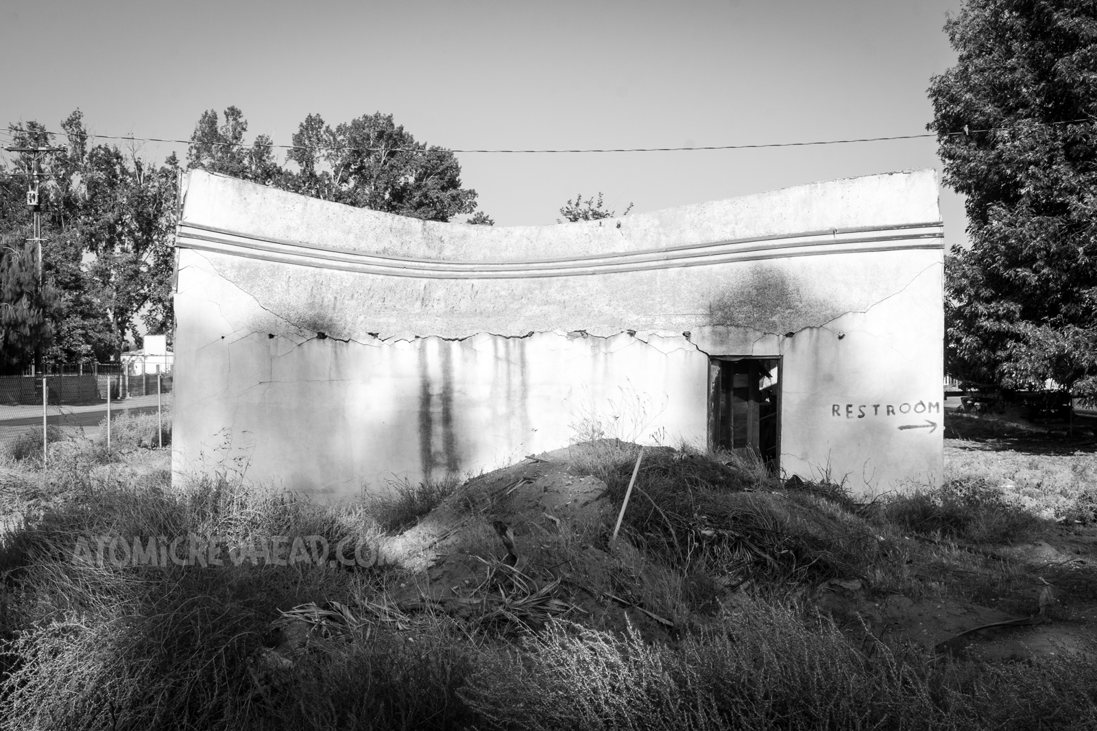 An abandoned and overgrown garage building with the top portion leaning backwards, about to collapse on itself.