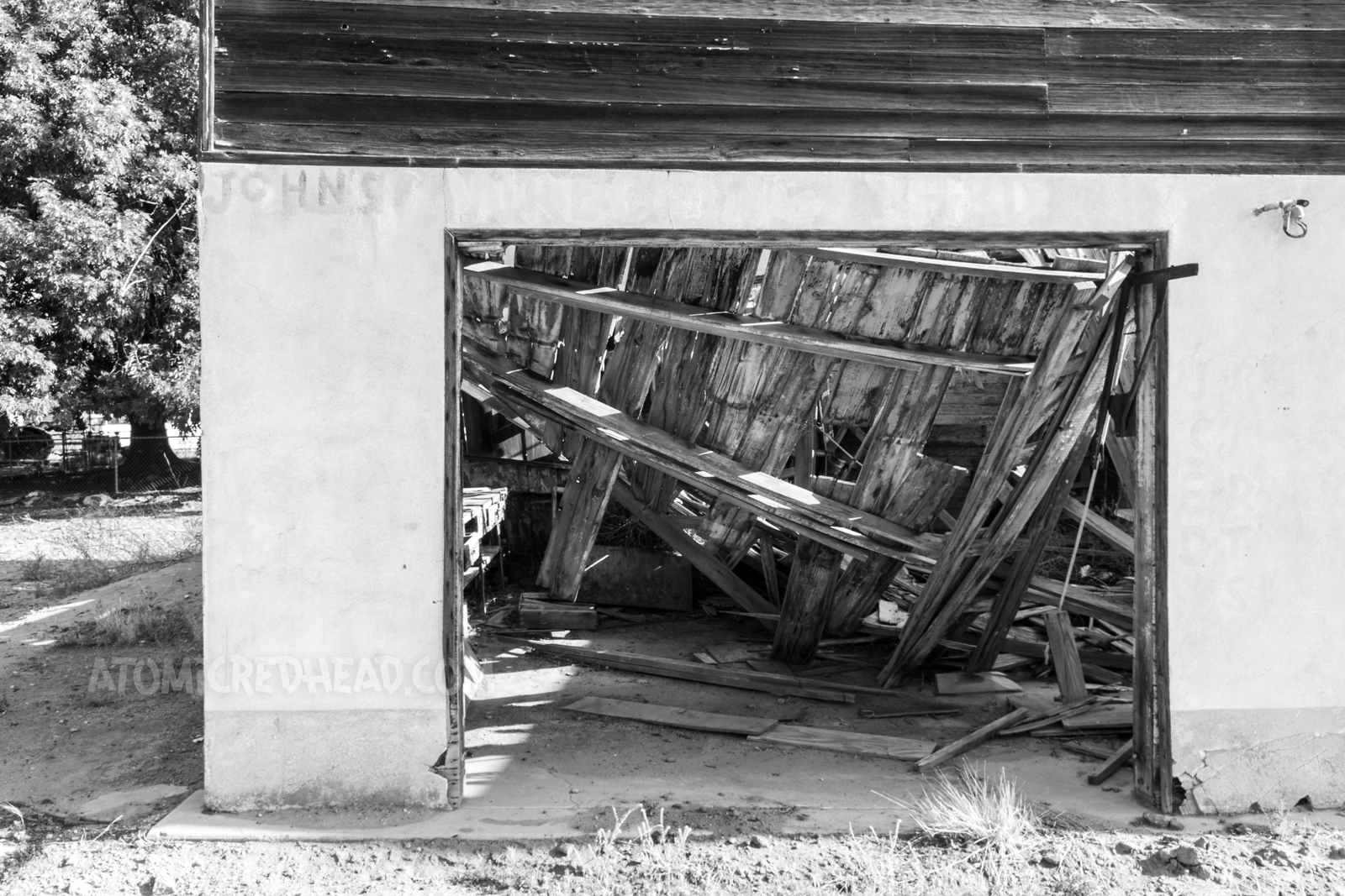 Close-up of the boards from the roof that now lay in various angles from falling in. Faded paint reads "John's" 