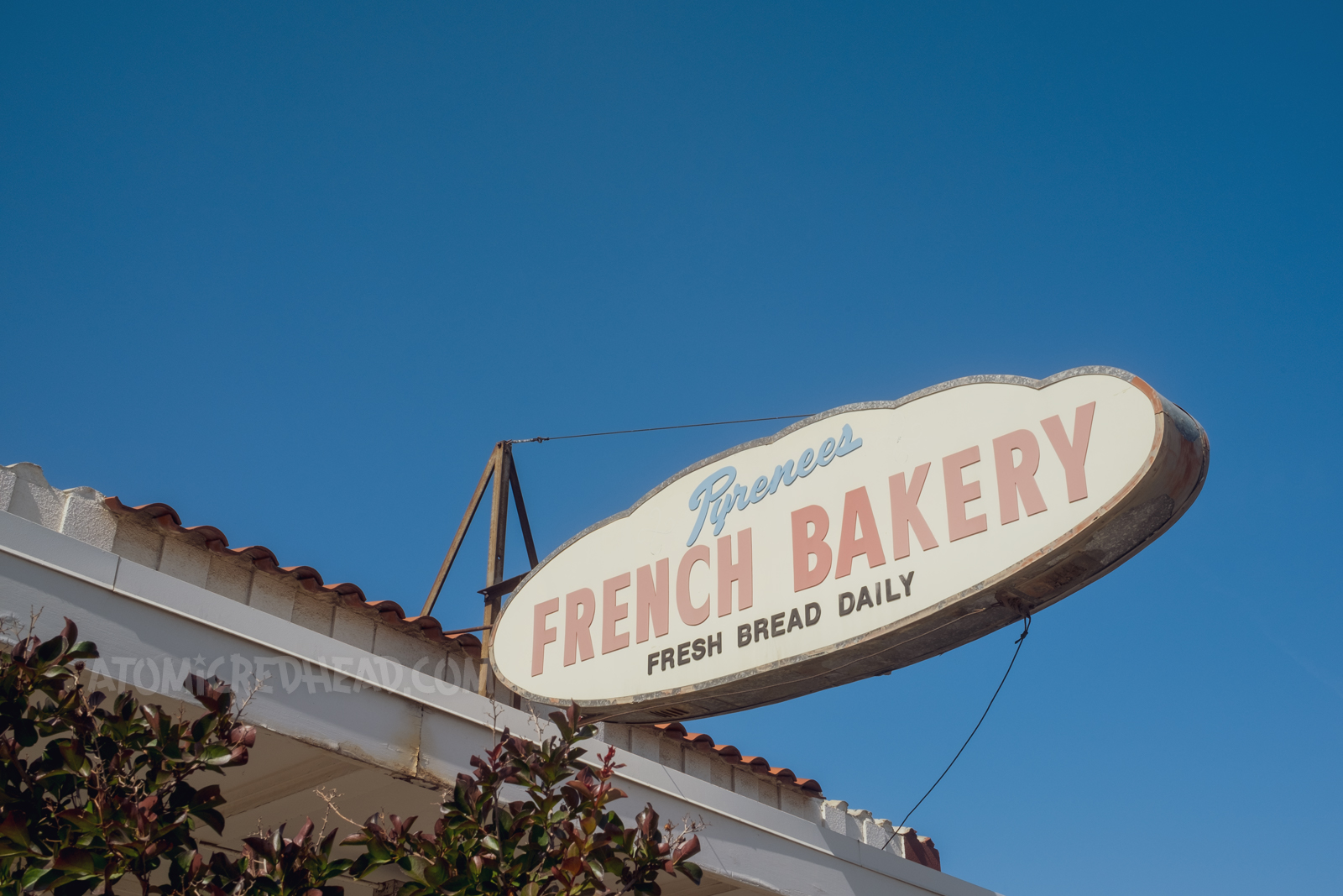 Backlit plastic sign that is shaped like a loaf of French bread, with text reading "Pyrenees French Bakery Fresh Bread Daily"