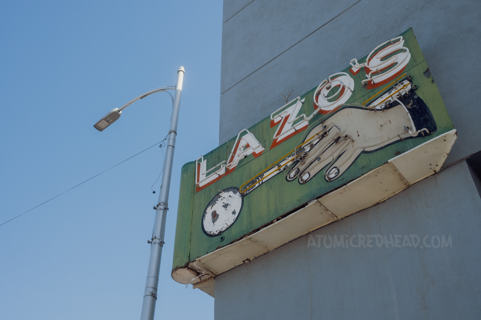 Neon sign on the corner of a building reading "Lazo's" and features a hand aiming a billiard cue at a ball. 