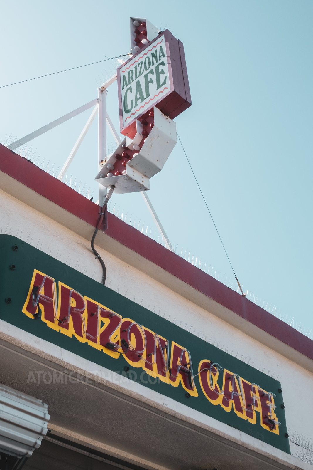 Signage for the Arizona Cafe. An arrow with a backlit plastic sign sits on the roof, a red, yellow, and green neon sign reading "Arizona Cafe" faces the front of the cafe.