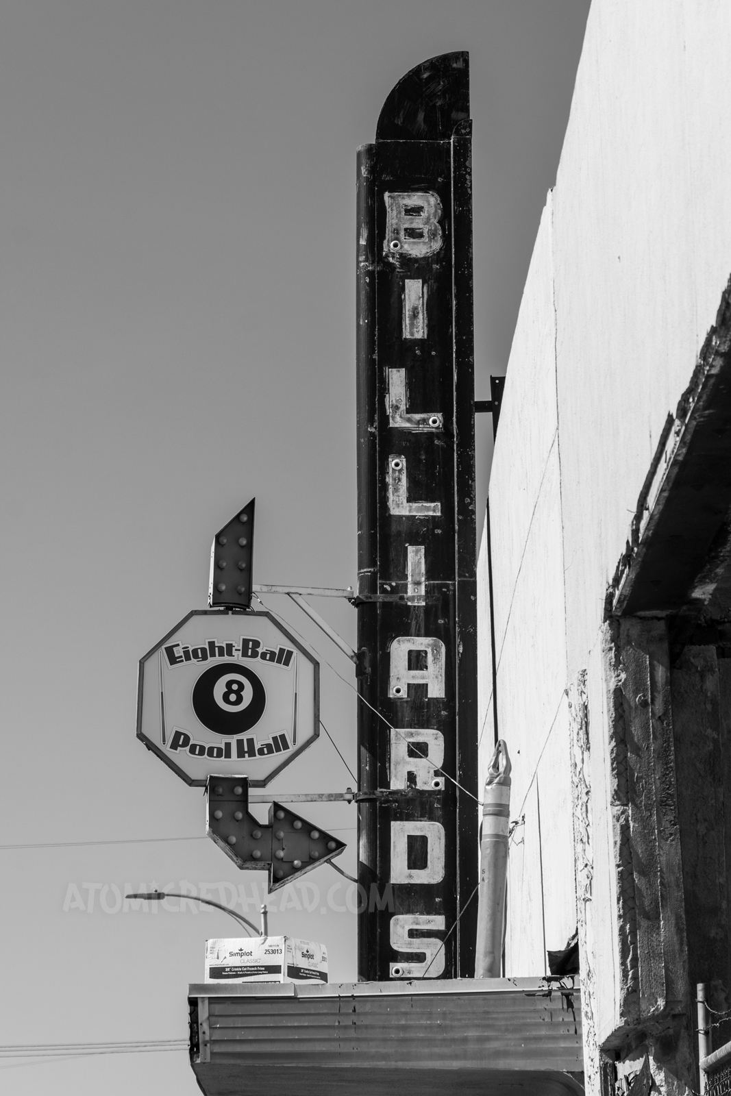 Blade style sign for a billiard hall, reading "Billiards" down in neon, an arrow next to it has a backlit plastic sign reading "Eight Ball Pool Hall" and features an eight ball.