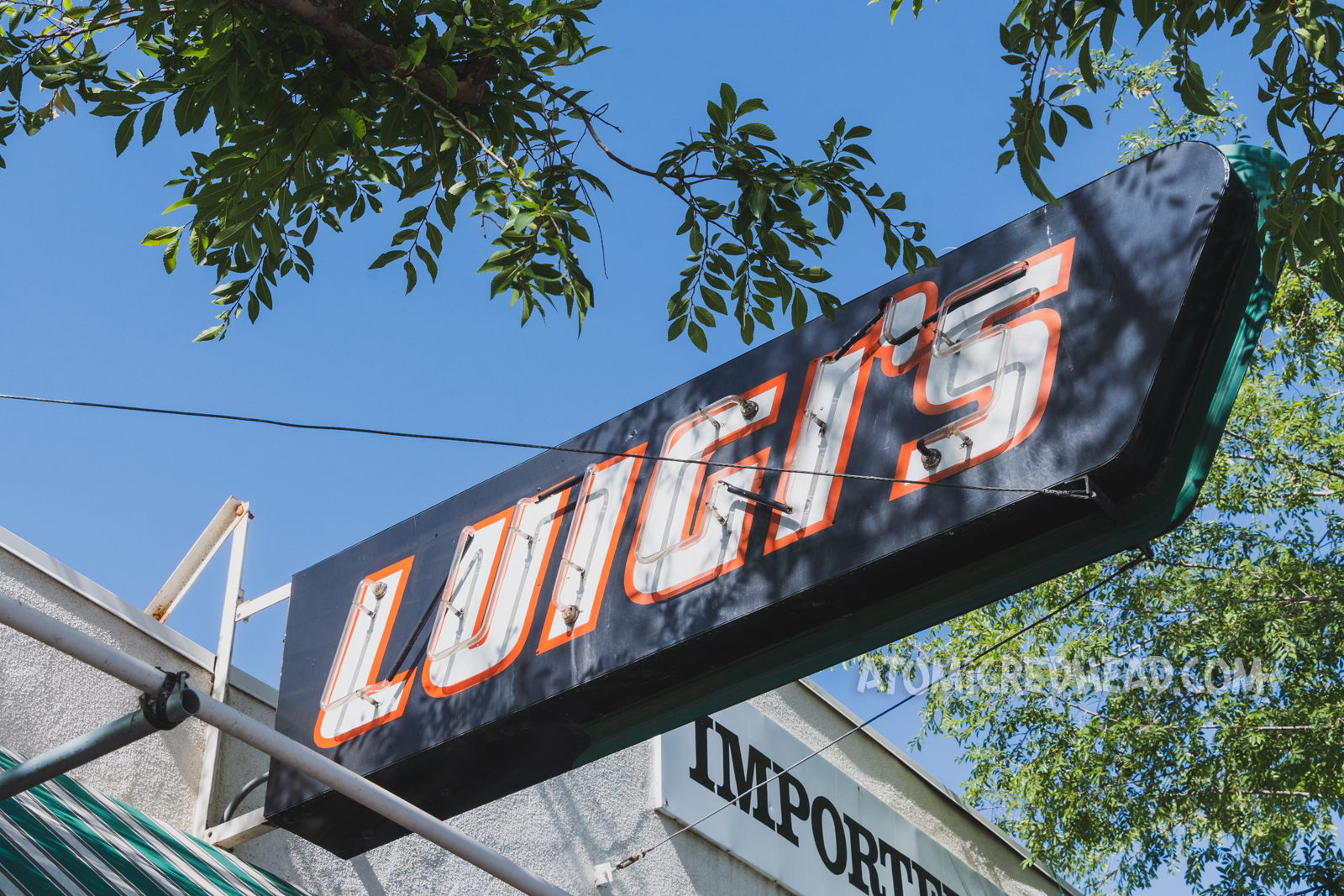 A small red, white, and black neon sign simply reads "Luigi's"