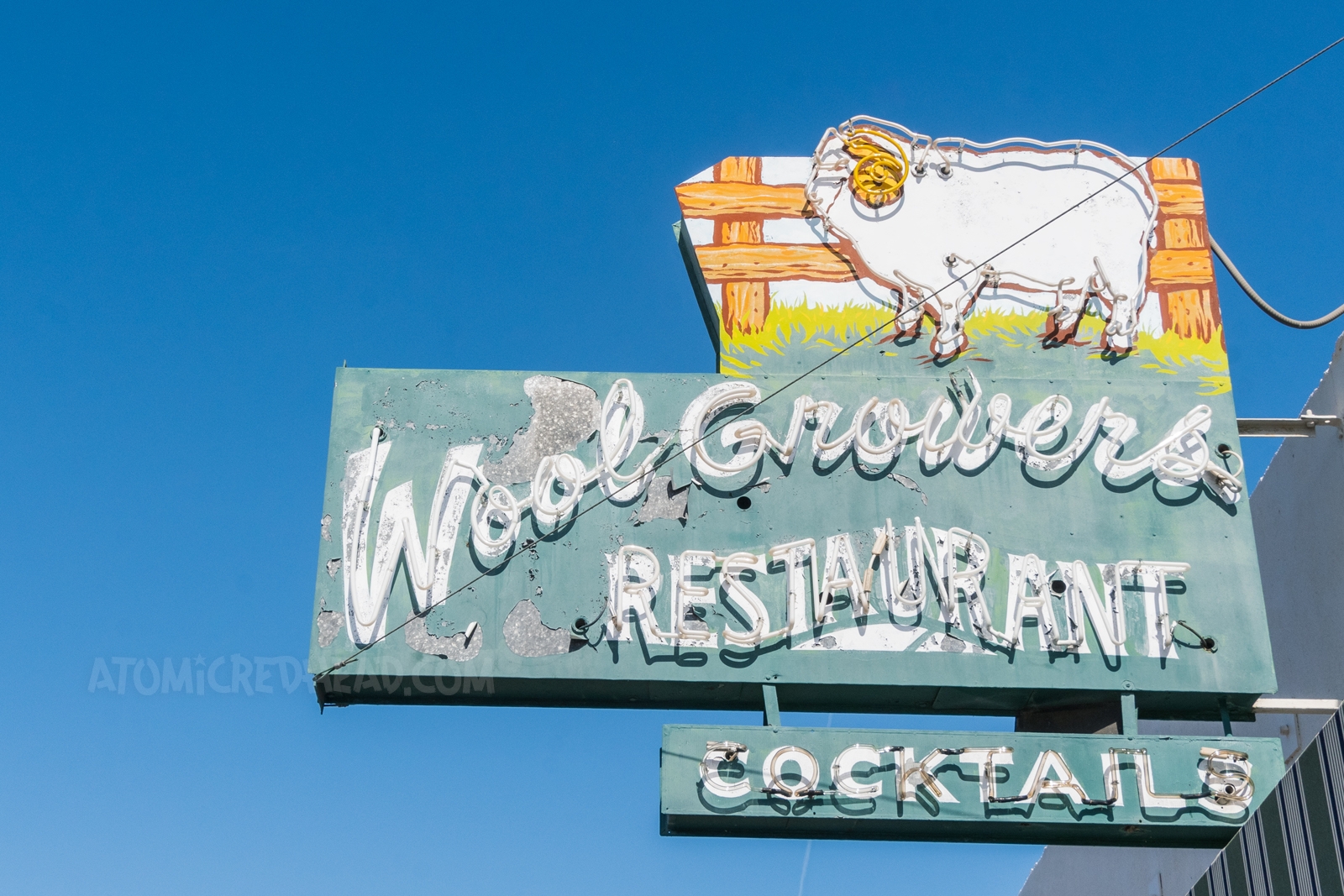 A green neon sign reads "Wool Growers Restaurant Cocktails" and features a sheet by a fence.